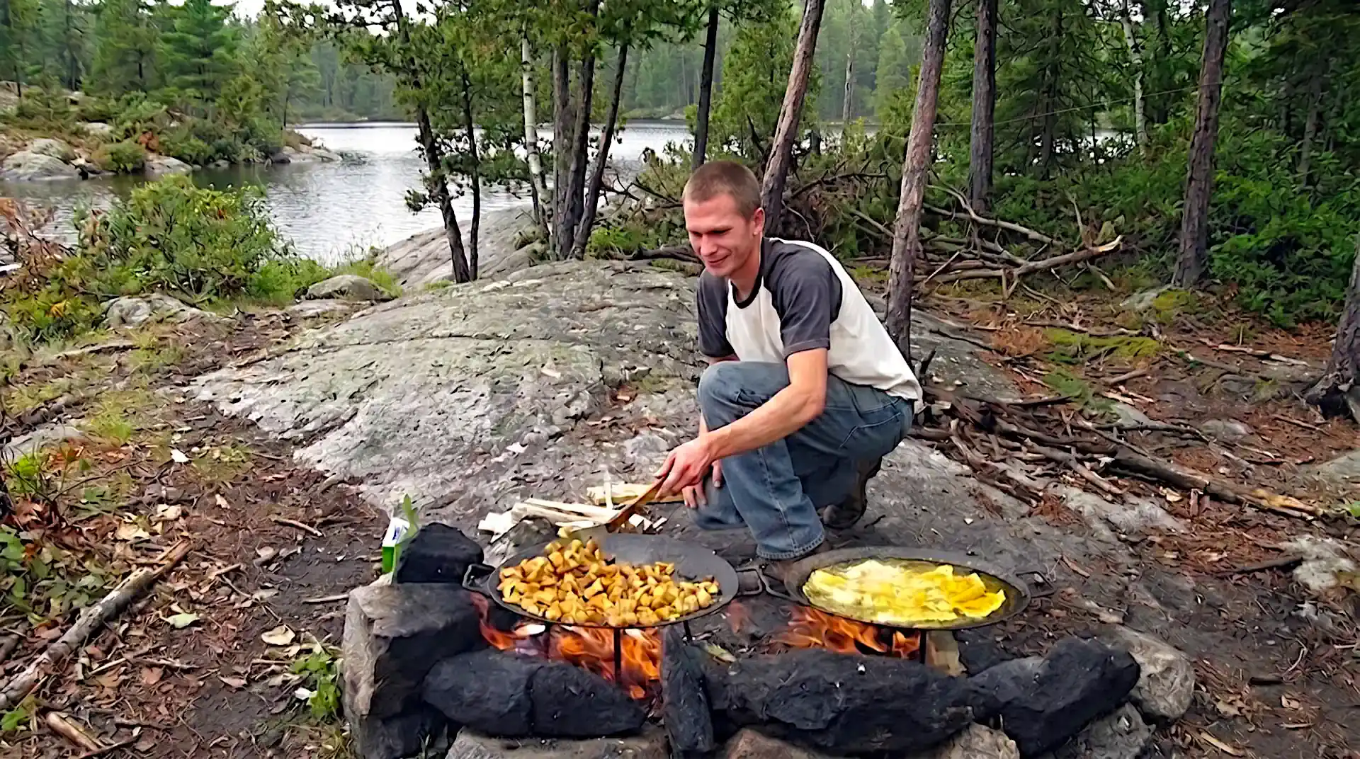 Fresh walleye fillets and potatoes frying in cast iron skillets over campfire coals beside a remote Canadian lake.