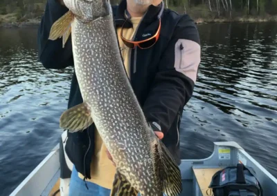 Angler holding a large Northern Pike on a boat with dark, dramatic storm clouds in the background in Manitoba.