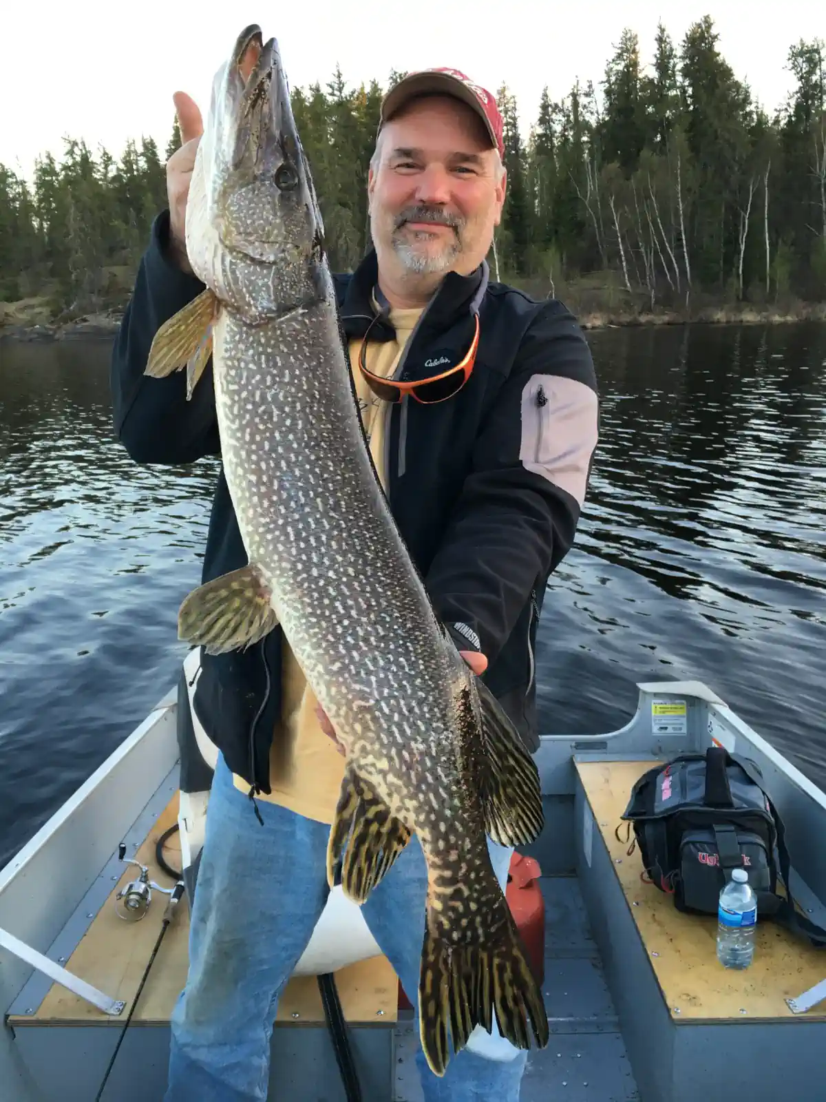 Angler holding a large Northern Pike on a boat with dark, dramatic storm clouds in the background in Manitoba.
