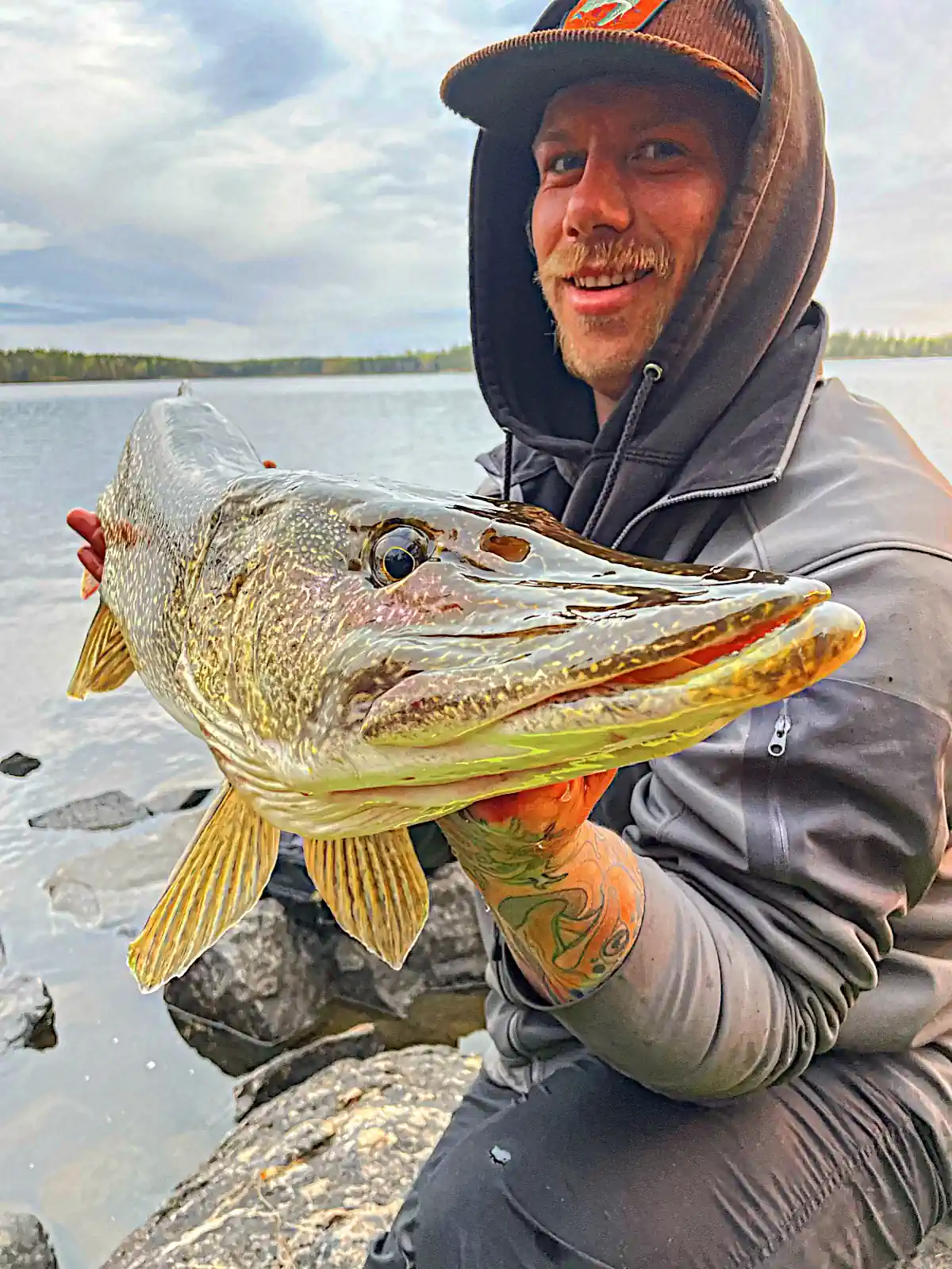 Fisherman holding a giant Northern Pike on a boat surrounded by morning mist on a Manitoba lake.