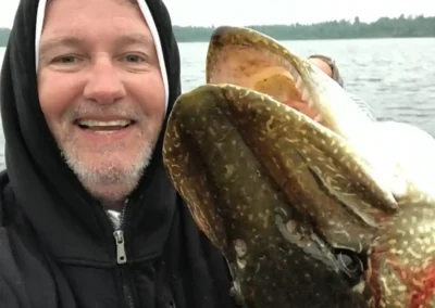 Angler holding a giant Northern Pike close to the camera lens, emphasizing the large head and teeth in Manitoba.