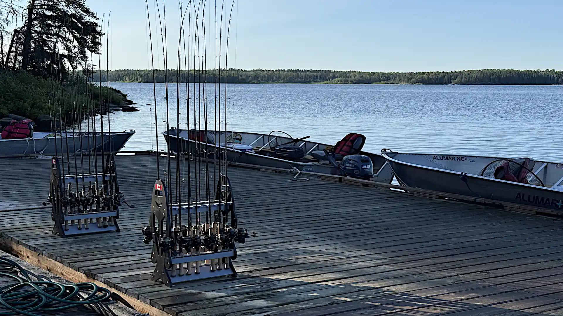 Two fully loaded rod racks sit on a wooden dock next to moored aluminum fishing boats on a calm river at Cobham River Lodge.