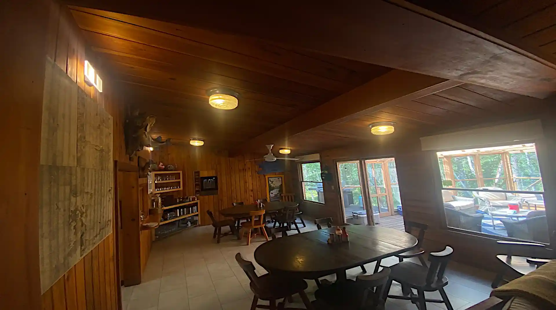 A wide interior view of the rustic, wood-paneled dining room at Cobham River Lodge, featuring dark wooden dining tables and glass doors leading to a bright, screened-in porch.