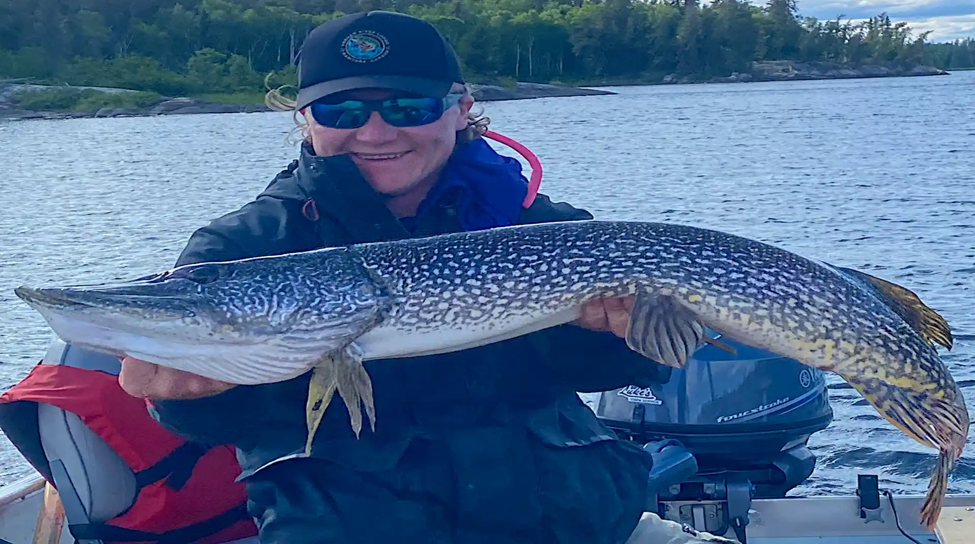 Smiling angler holding a very long 40-plus inch Northern Pike horizontally in a boat in Manitoba.