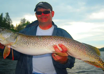 Fisherman holding a massive Northern Pike silhouetted against a vibrant Manitoba sunset.