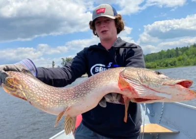 Fisherman on a boat holding a large trophy Northern Pike with both hands in Manitoba, Canada.