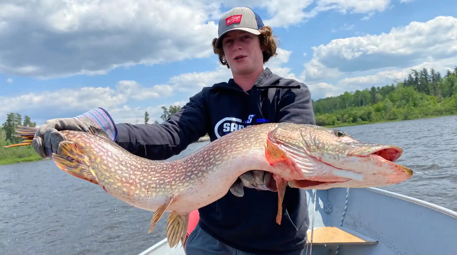 Fisherman on a boat holding a large trophy Northern Pike with both hands in Manitoba, Canada.